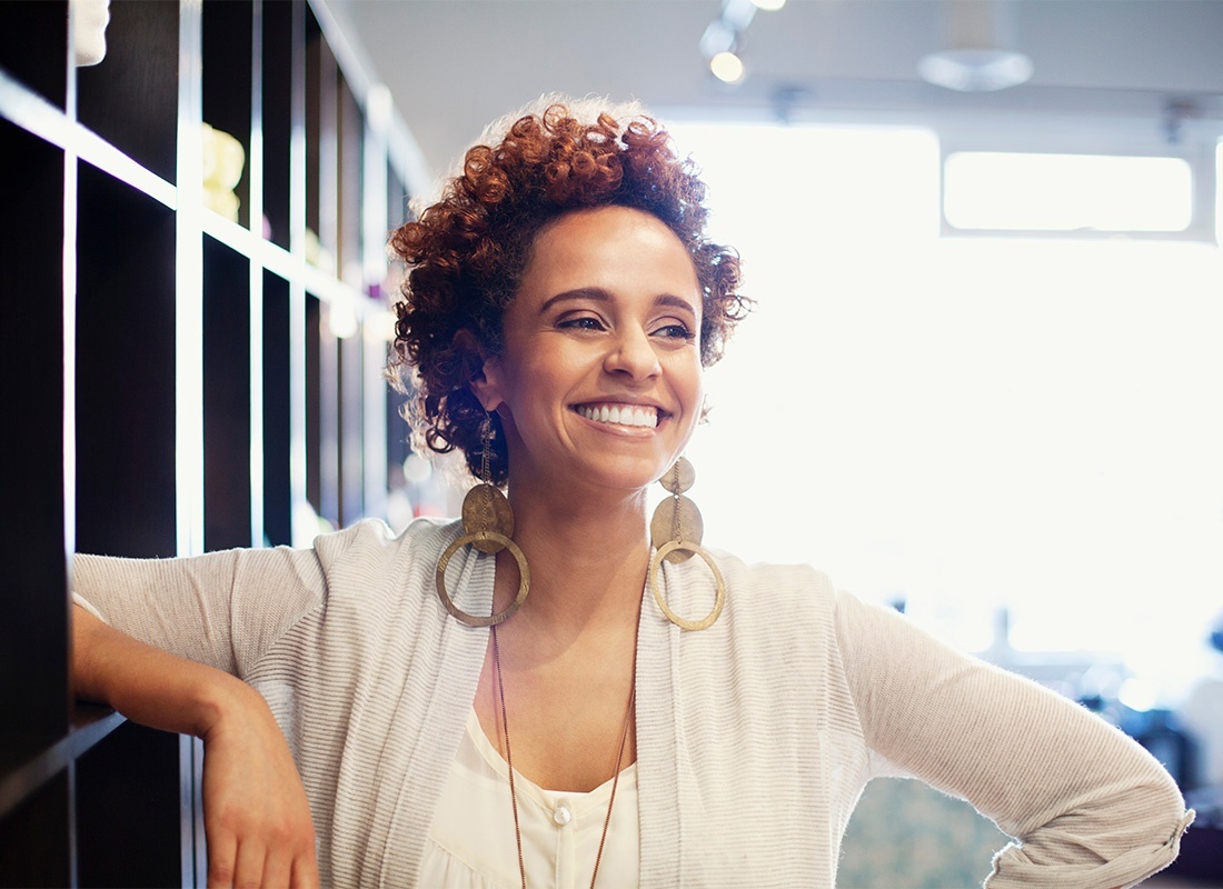 Business Insurance - Closeup Portrait of a Cheerful Young African American Female Business Owner Standing Next to Shelves in a Bright Office