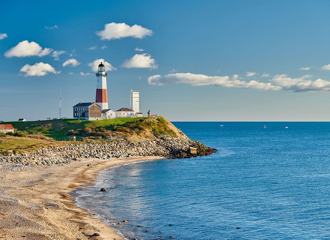 Contact - Scenic View of a Lighthouse on the Coast Against a Cloudy Blue Sky in Long Island New York on a Sunny Day