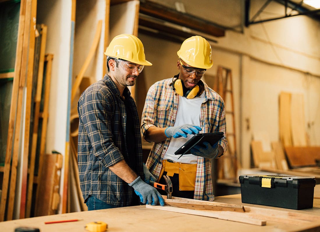 Insurance by Industry - Two Young Male Contractors Working with Wood and Looking at a Tablet While Standing Inside a Workshop