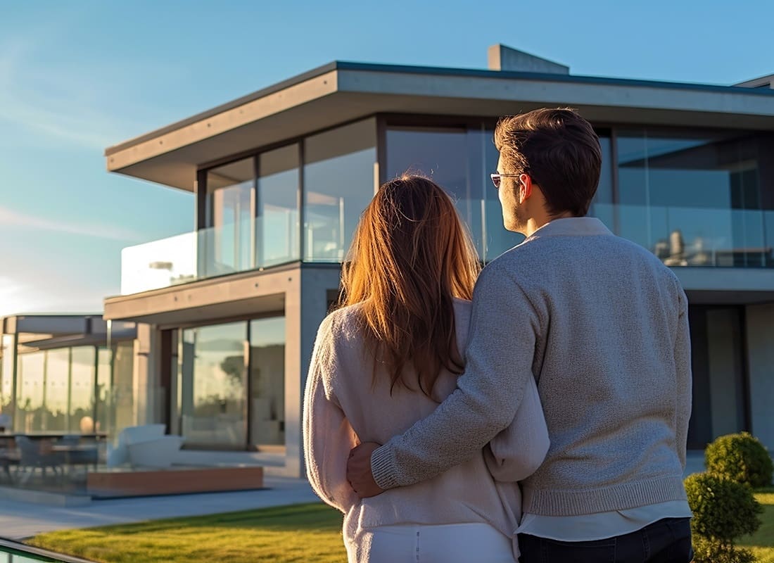 Personal Insurance - Rear View of a Married Couple Standing Outside Looking at Their New Modern Two Story Luxury Home at Sunset